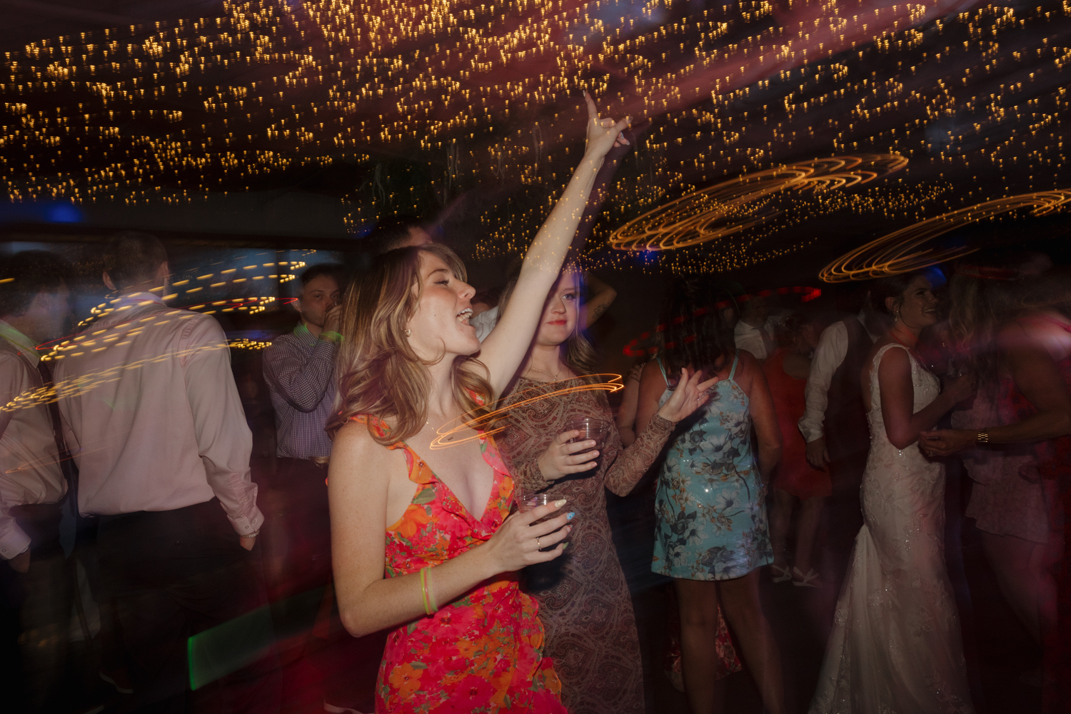 Guest singing and raising her hand on the dance floor at Boxed and Burlap Delavan with dramatic light trails overhead.