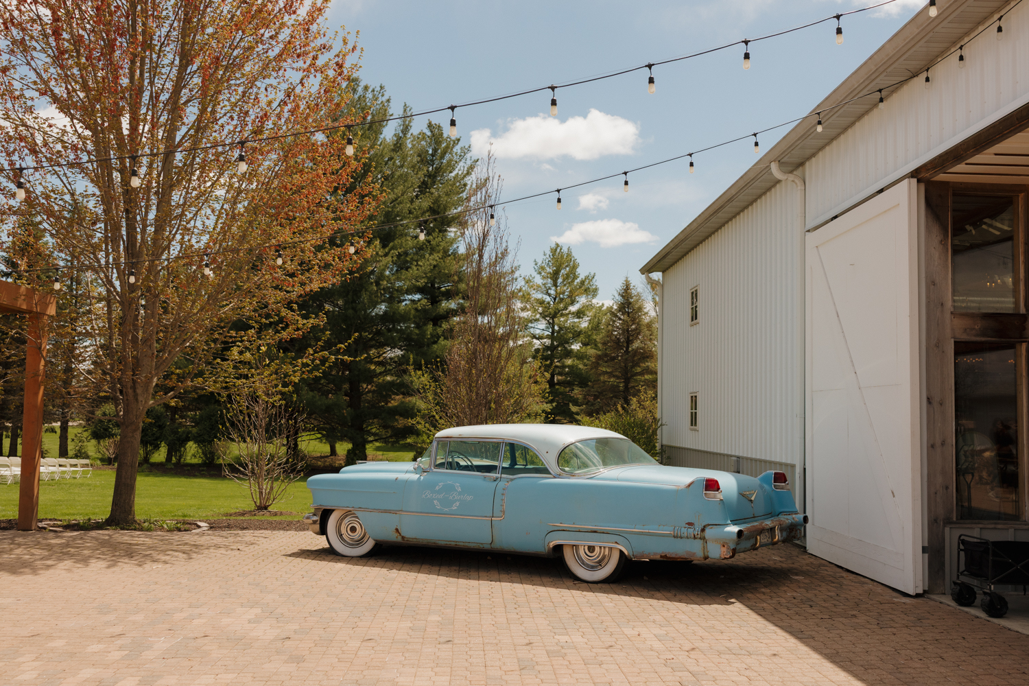 Vintage blue car parked outside Boxed and Burlap Delavan beneath café string lights on a sunny afternoon.