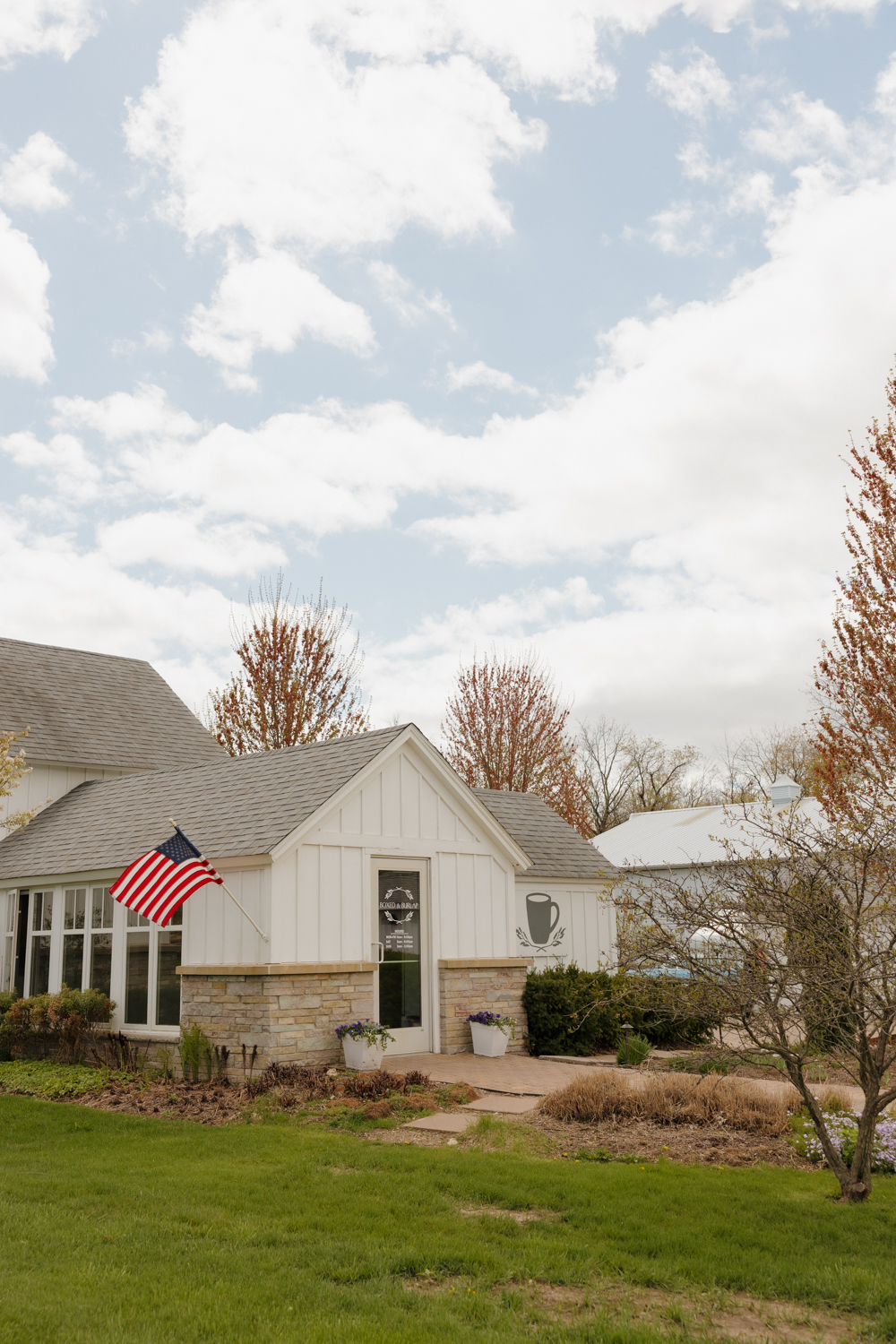 Exterior of Boxed and Burlap Delavan with white siding, landscaped greenery, and an American flag near the entrance.