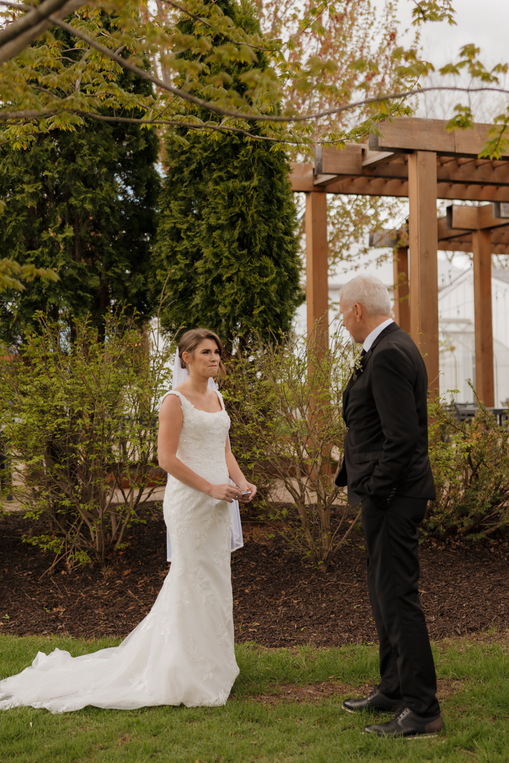 Bride sharing a first look with her father beneath the wooden pergola at Boxed and Burlap Delavan.