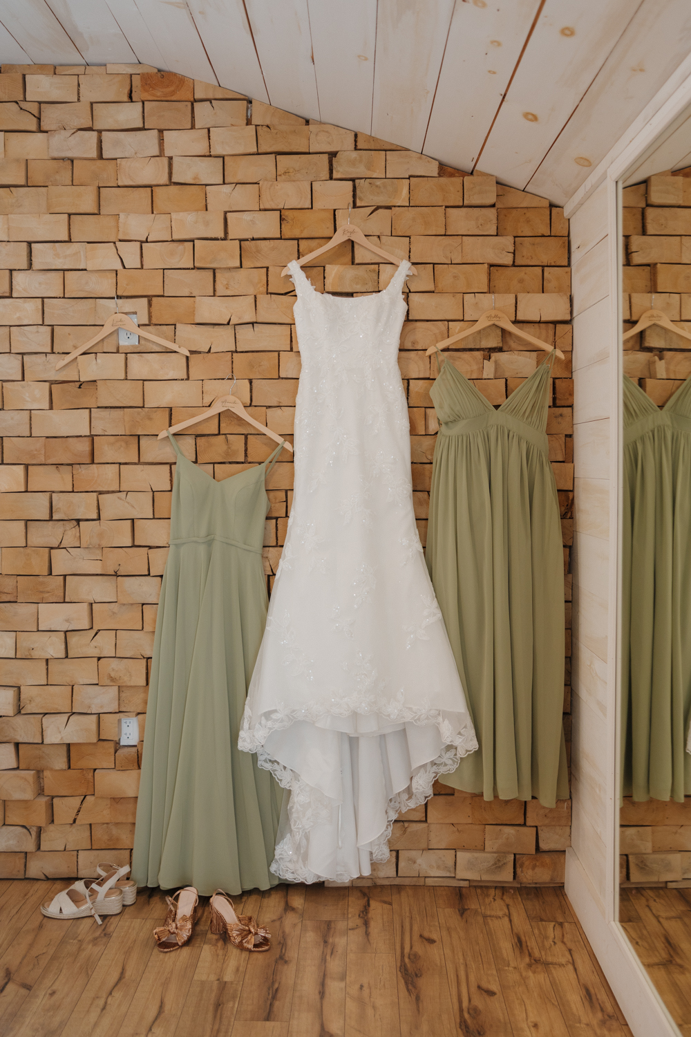Bride’s lace wedding dress hanging between sage green bridesmaid dresses inside Boxed and Burlap Delavan.