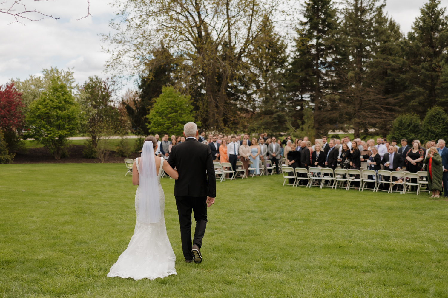 Bride walking down the outdoor aisle at Boxed and Burlap Delavan with guests standing on either side of the lawn.