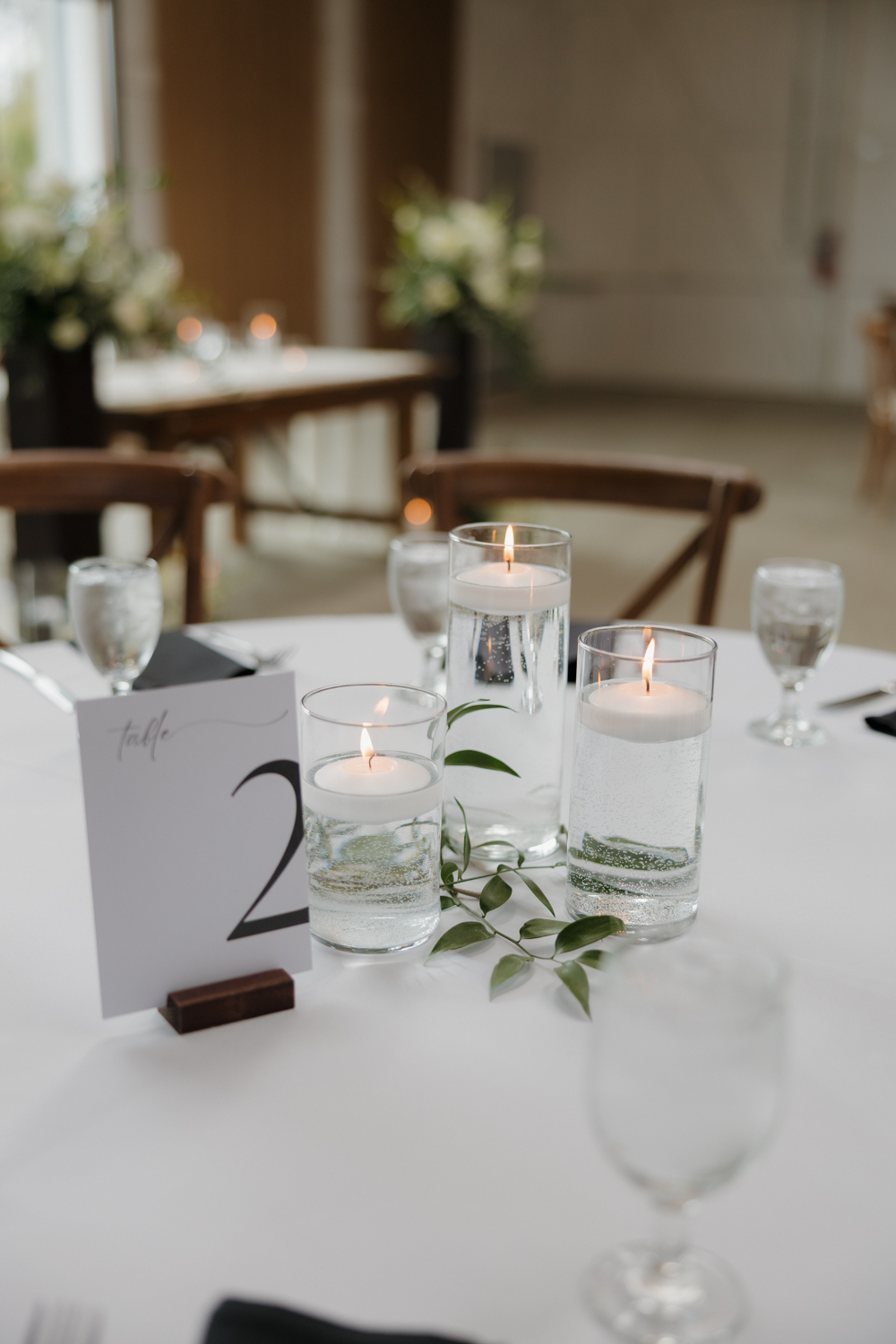 Reception table detail with floating candles, greenery, and modern table number design.