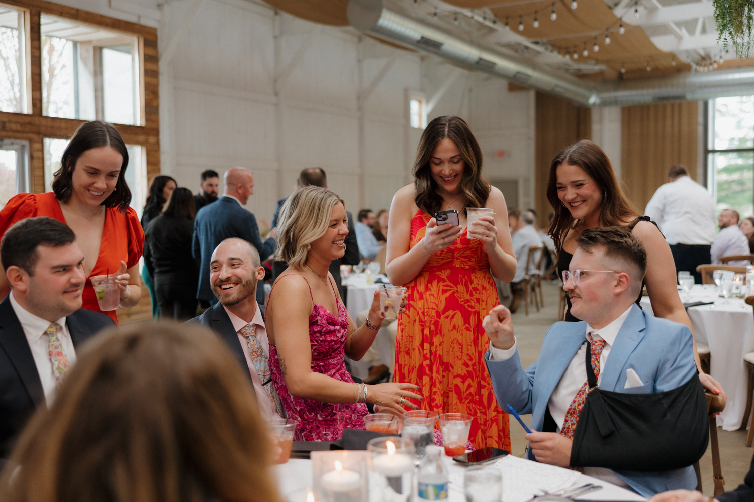 Guests gathered around a reception table laughing and sharing drinks during the celebration.