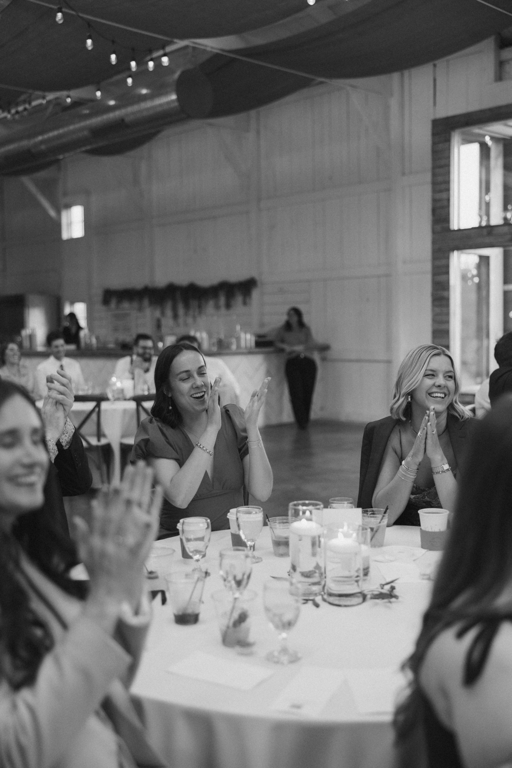 Wedding guests clapping and smiling at their tables inside Boxed and Burlap Delavan during the reception.