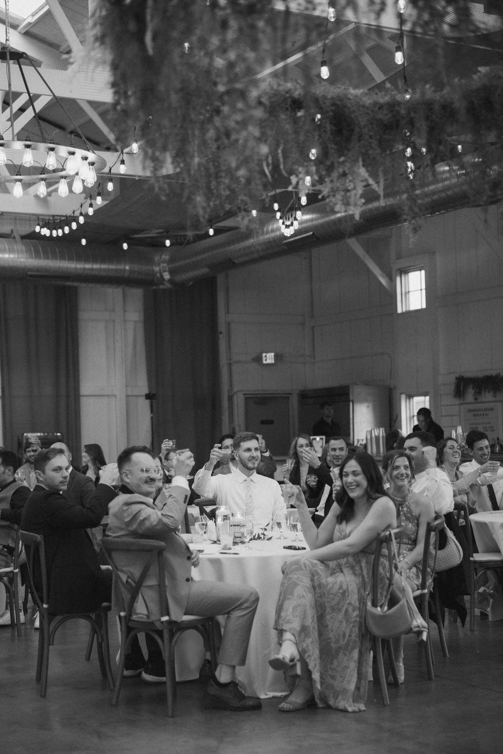 Wedding guests raising their glasses in a toast inside Boxed and Burlap Delavan beneath string lights and greenery.