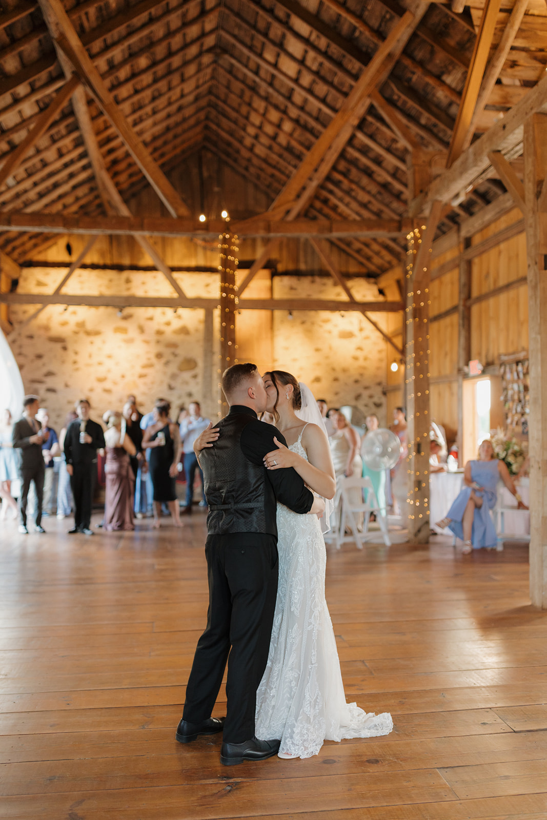 Bride and groom sharing their first dance inside a rustic barn reception space with warm string lights, photographed by a madison wisconsin wedding photographer.