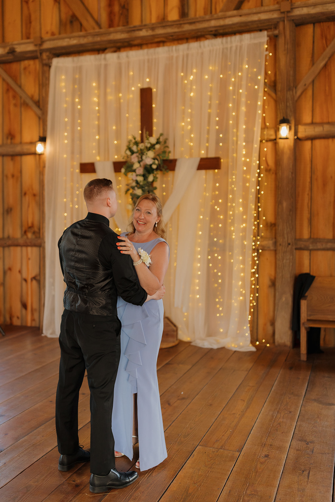 A mother and son slow dance during a wedding reception in a rustic barn with glowing string lights, photographed by a madison wisconsin wedding photographer.