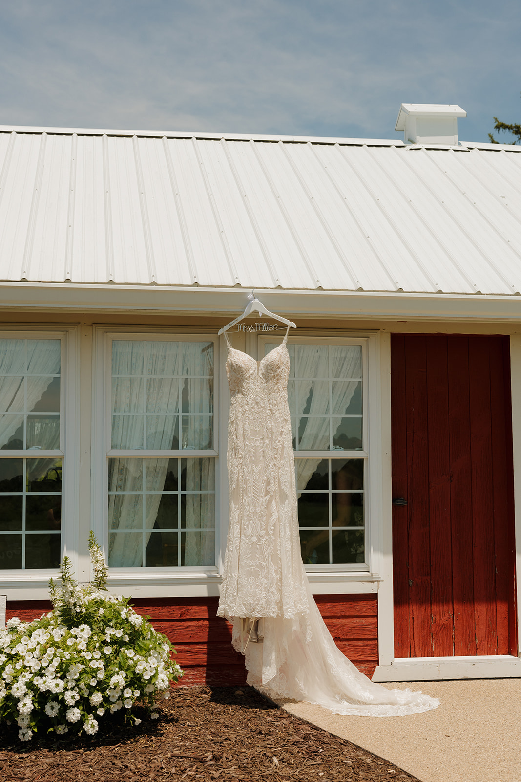 Lace wedding dress hanging outside a red barn window on a sunny day, photographed by a madison wisconsin wedding photographer.
