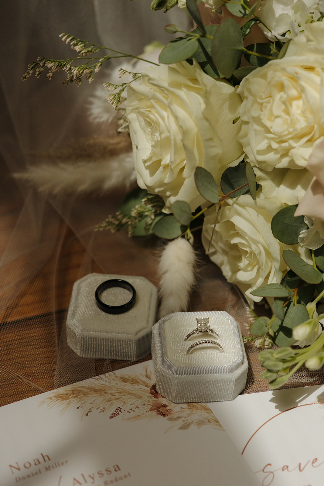 Close-up of wedding rings in velvet boxes styled beside white roses and invitations, photographed by a madison wisconsin wedding photographer.