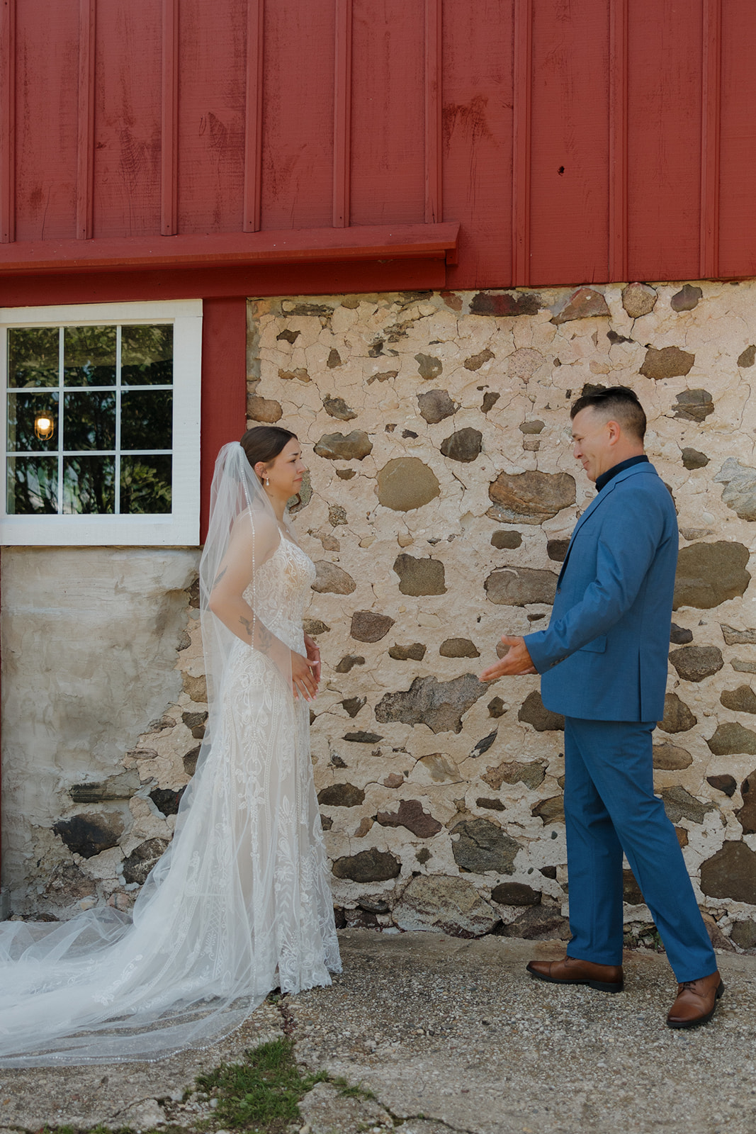 Bride and father of bride smiling at each other during their first look beside a red barn wall, captured by a madison wisconsin wedding photographer.