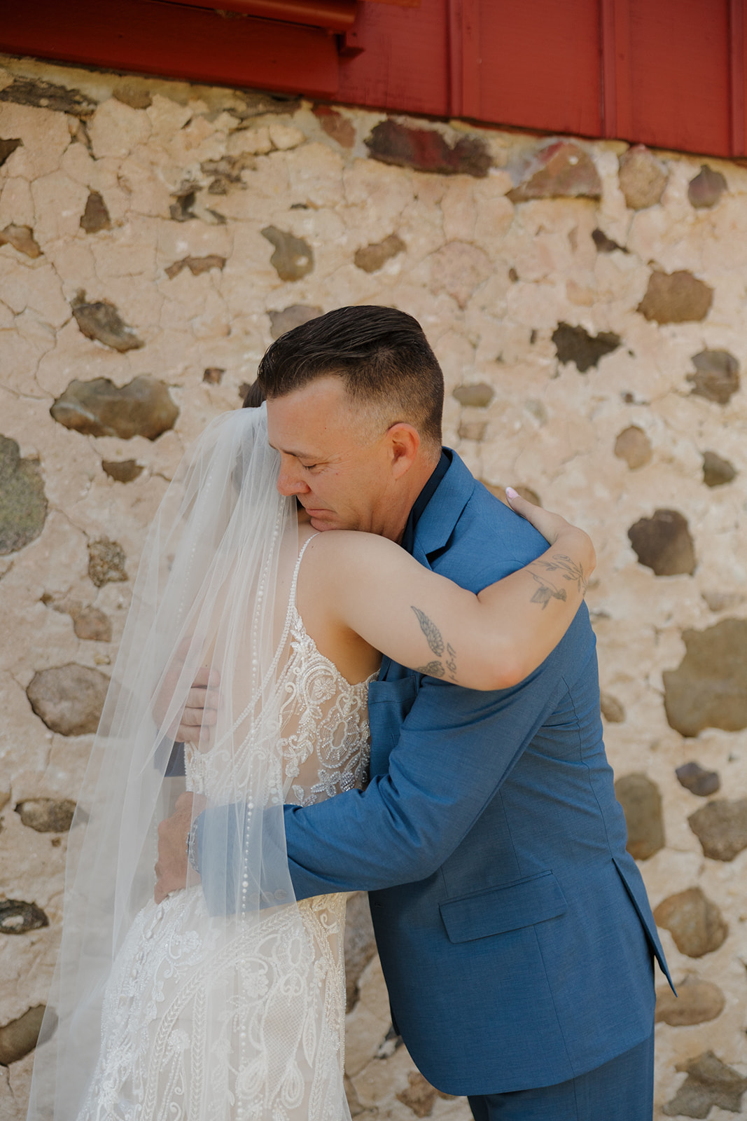 Bride and her father sharing an emotional hug during their first look in front of a rustic stone barn, photographed by a madison wisconsin wedding photographer.