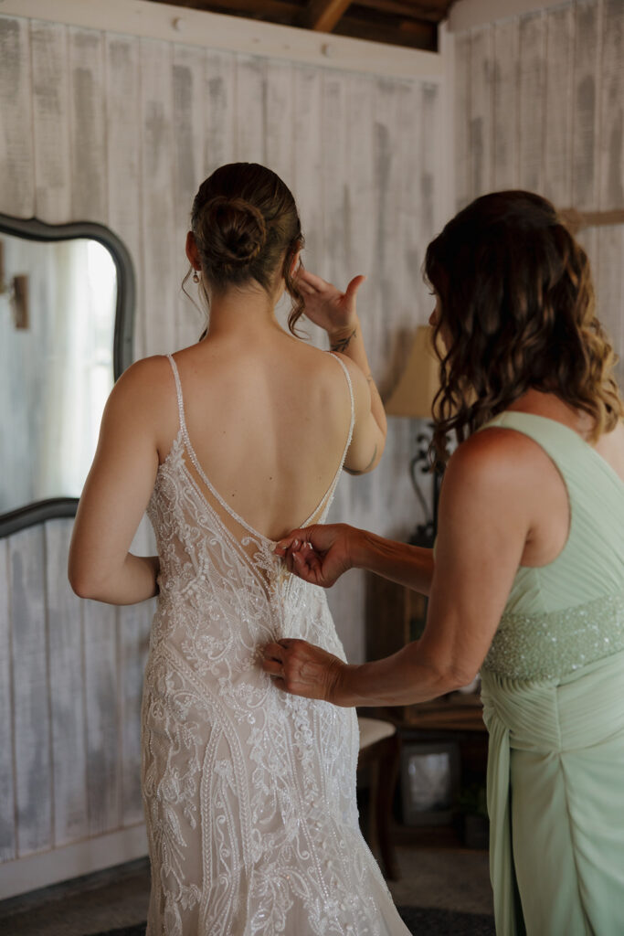 Mother helping zip the back of the bride’s lace wedding dress during getting ready, photographed by a madison wisconsin wedding photographer.
