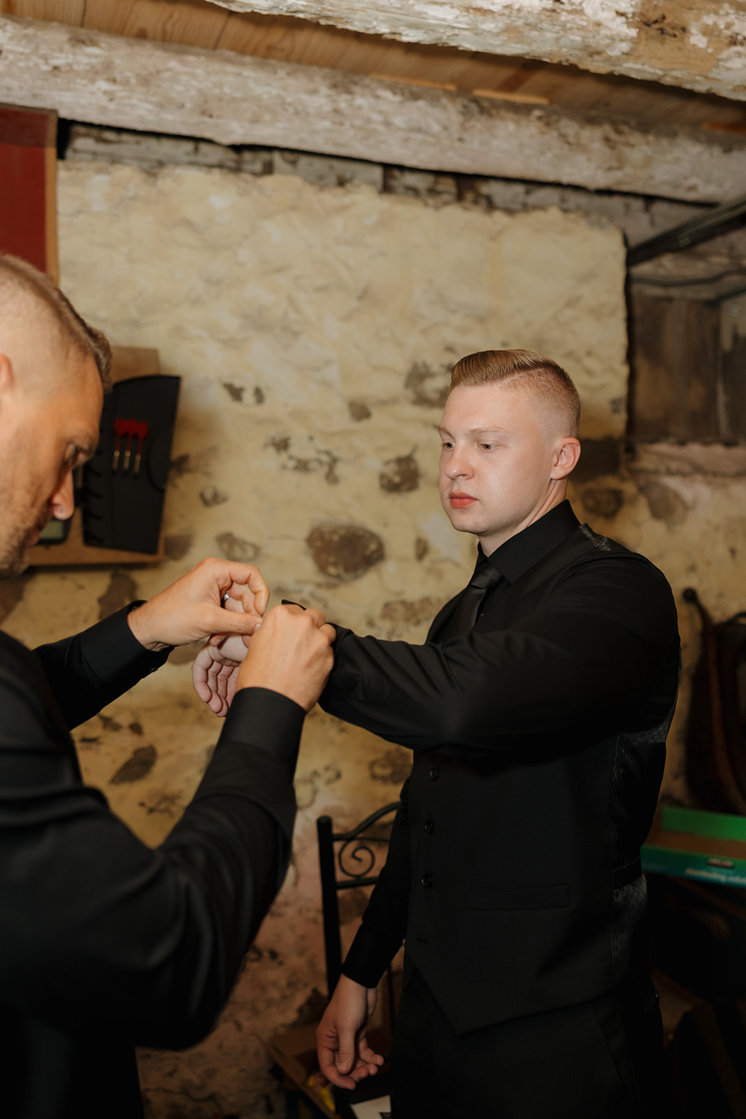 Groom getting help adjusting his sleeve while preparing for the wedding ceremony, photographed by a madison wisconsin wedding photographer.