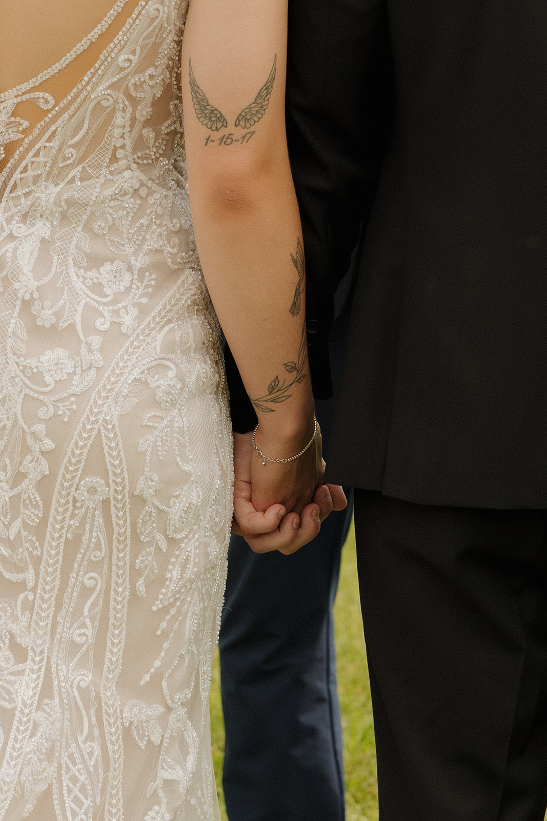 Close-up of bride and groom holding hands, highlighting lace dress details and wedding day tattoos, photographed by a madison wisconsin wedding photographer.