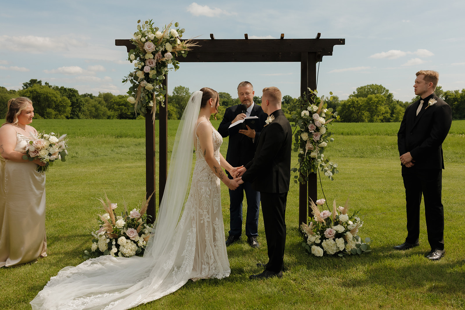 Bride and groom holding hands during an outdoor ceremony under a floral wooden arch, photographed by a madison wisconsin wedding photographer.