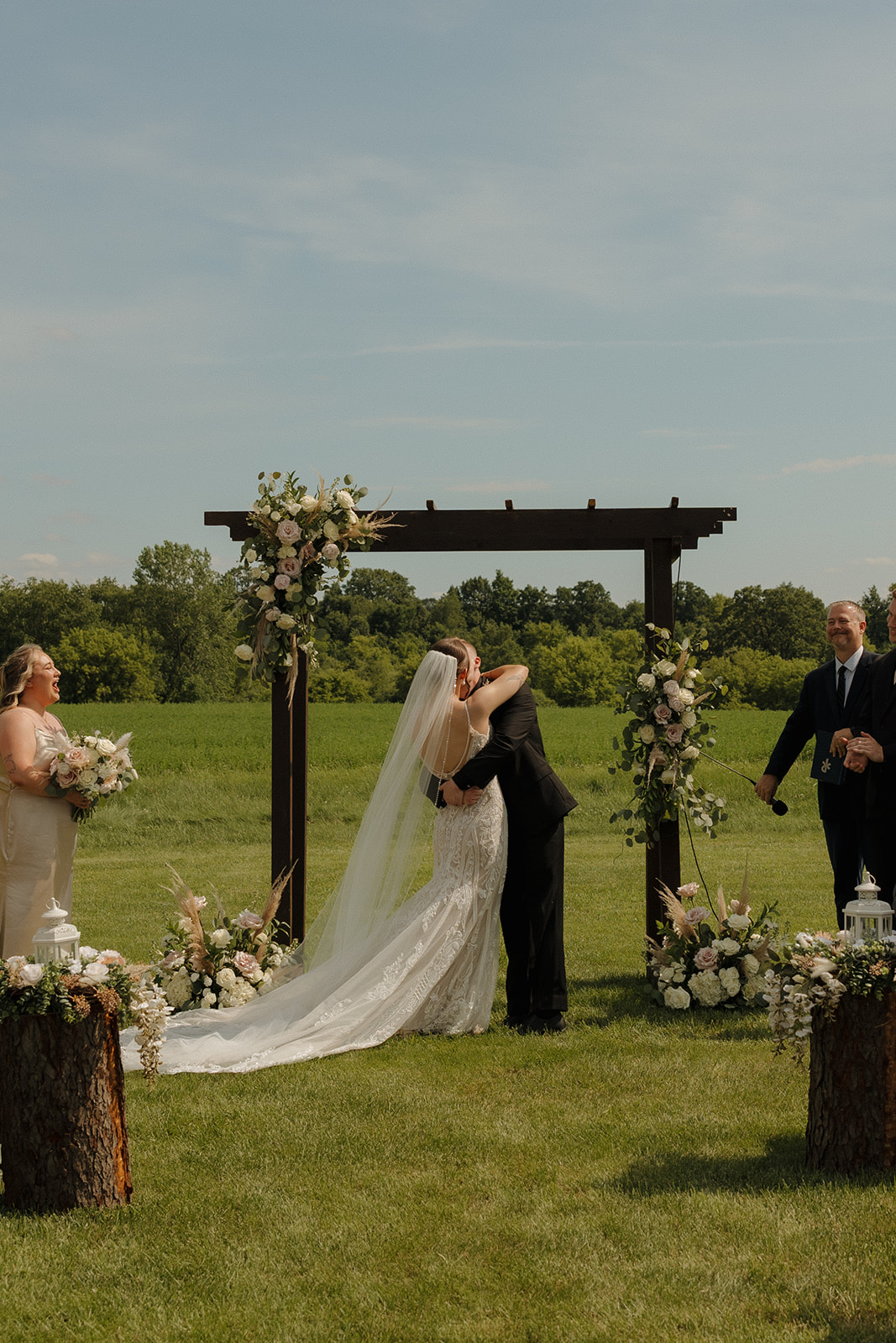 Bride and groom sharing their first kiss under a floral ceremony arch in an open field, photographed by a madison wisconsin wedding photographer.