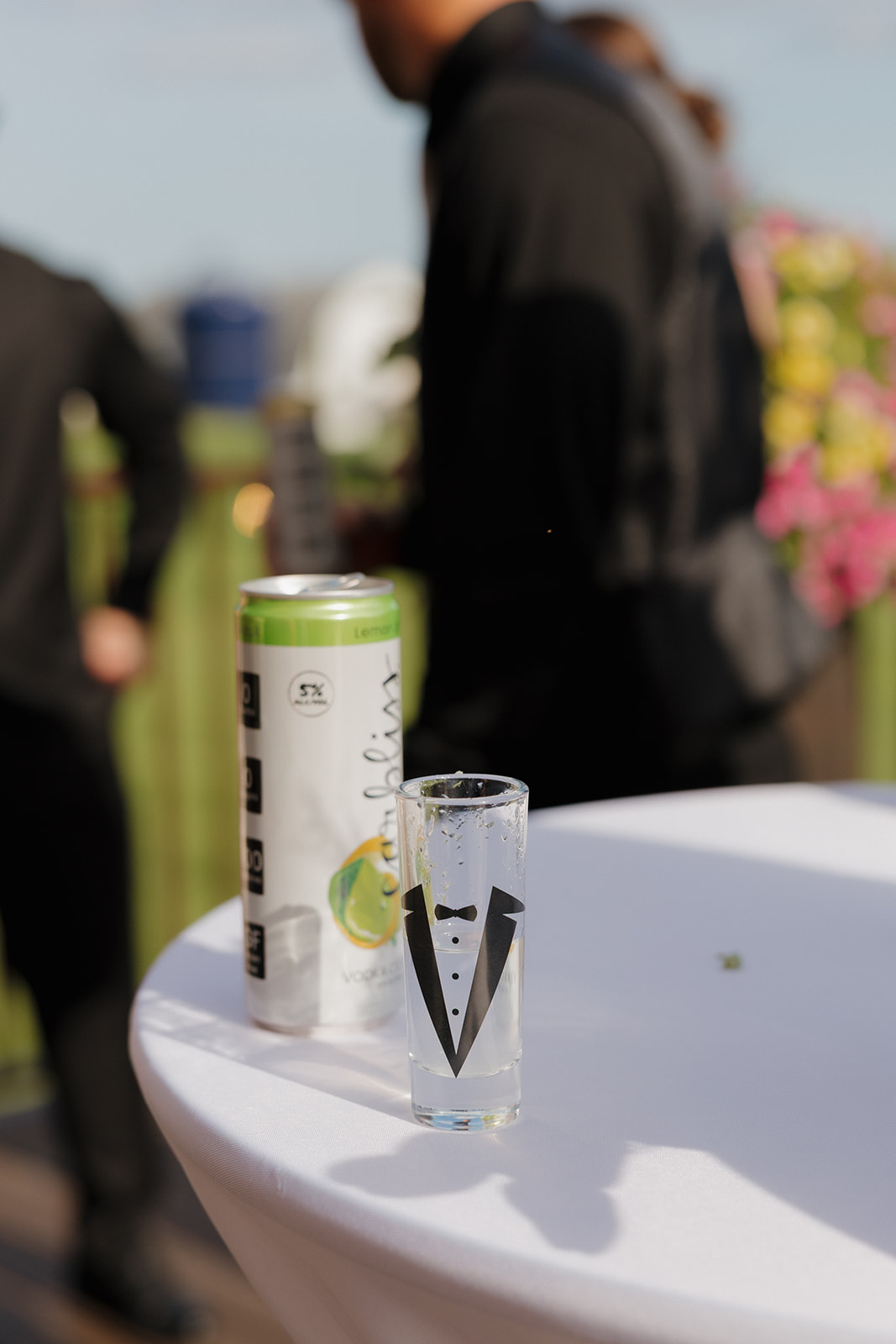 A cocktail table detail featuring a canned drink and a tuxedo-themed shot glass during an outdoor wedding cocktail hour, photographed by a madison wisconsin wedding photographer.