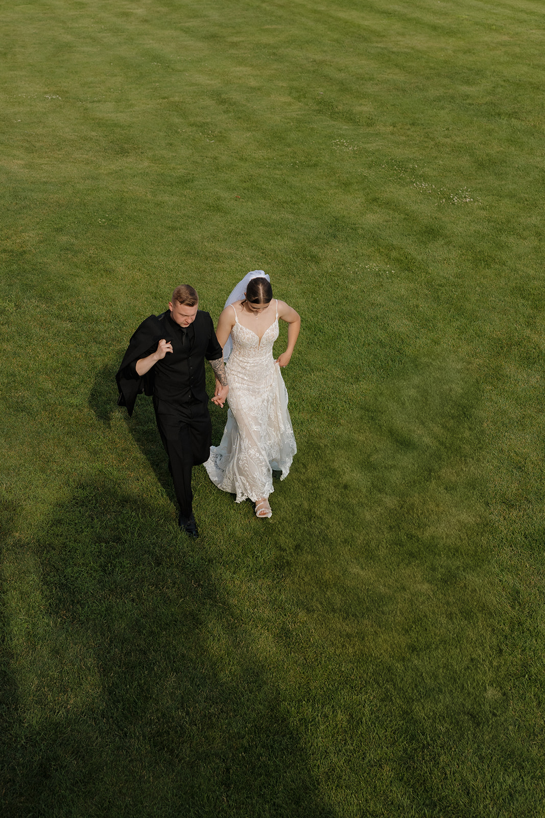 An overhead view of the bride and groom walking hand in hand across a lush green lawn, sharing a quiet moment together after the ceremony.