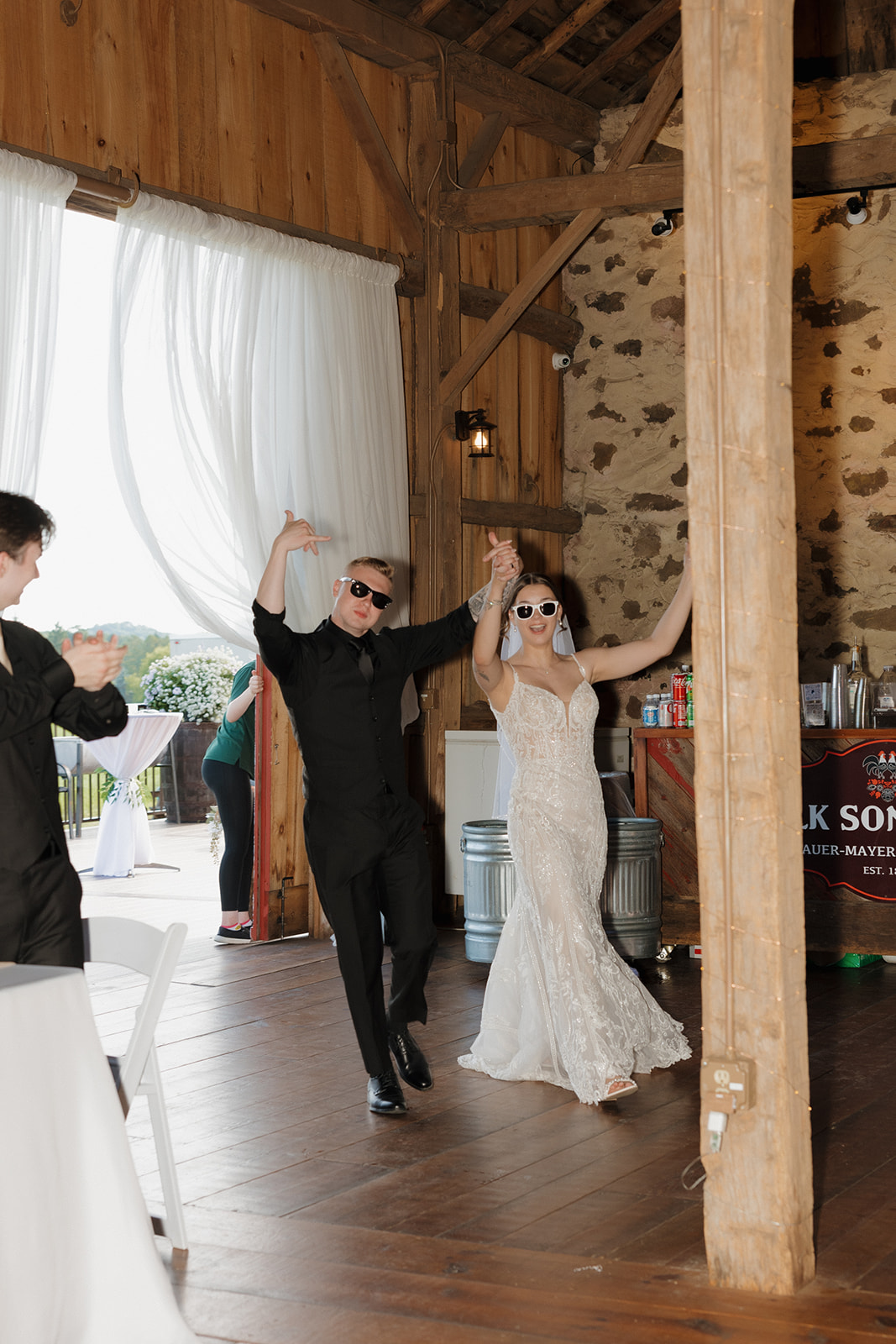 The bride and groom throw their hands up in celebration during their grand entrance at a barn wedding reception, captured by a madison wisconsin wedding photographer.