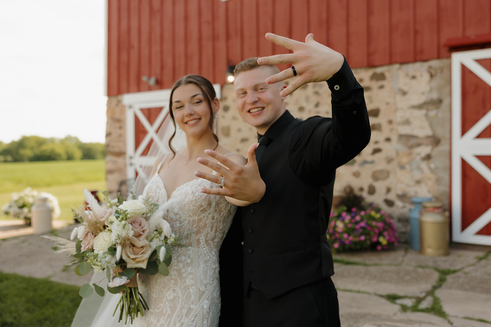 Bride and groom showing their wedding rings in front of a rustic barn, captured by a madison wisconsin wedding photographer.