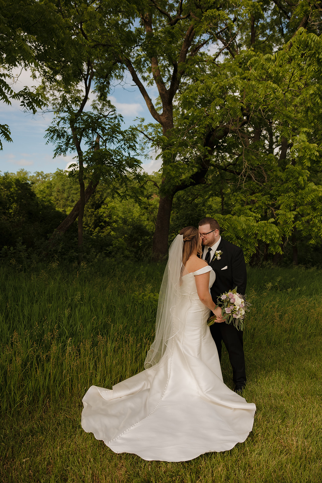 Bride and groom embracing under trees at an outdoor Wisconsin wedding ceremony site