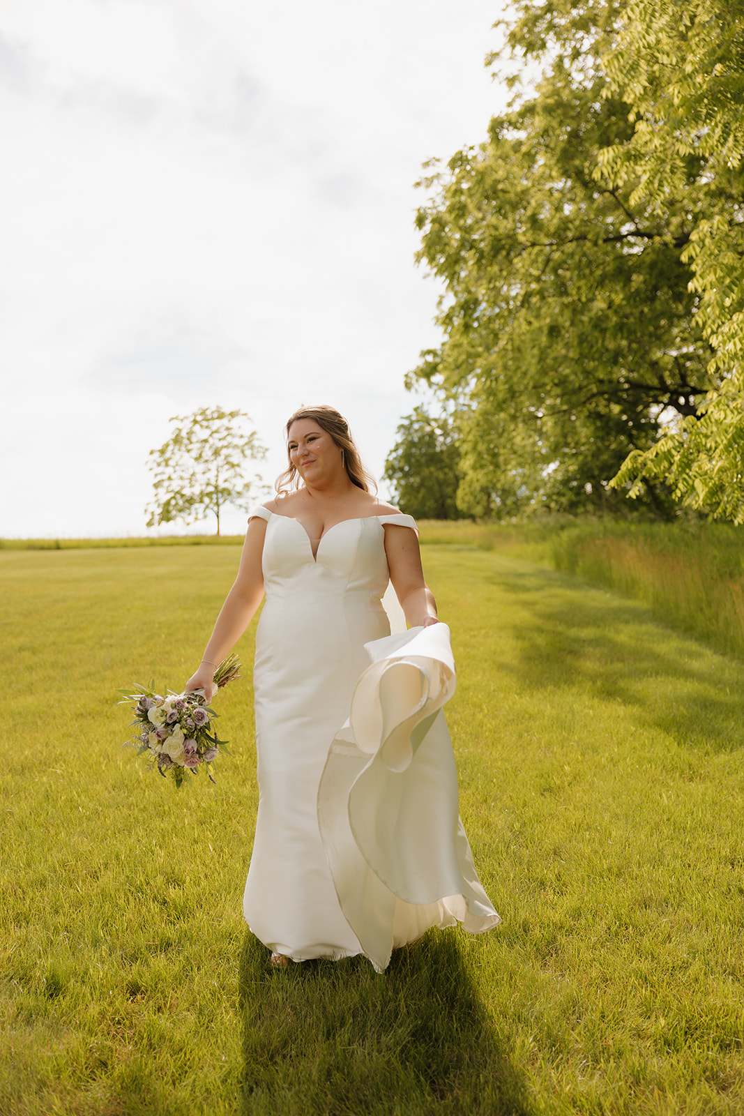Bride walking through open field in wedding dress during golden hour
