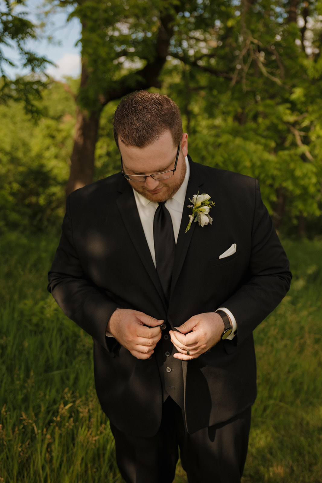 Groom buttoning black suit jacket in golden hour light at wedding venues in Wisconsin