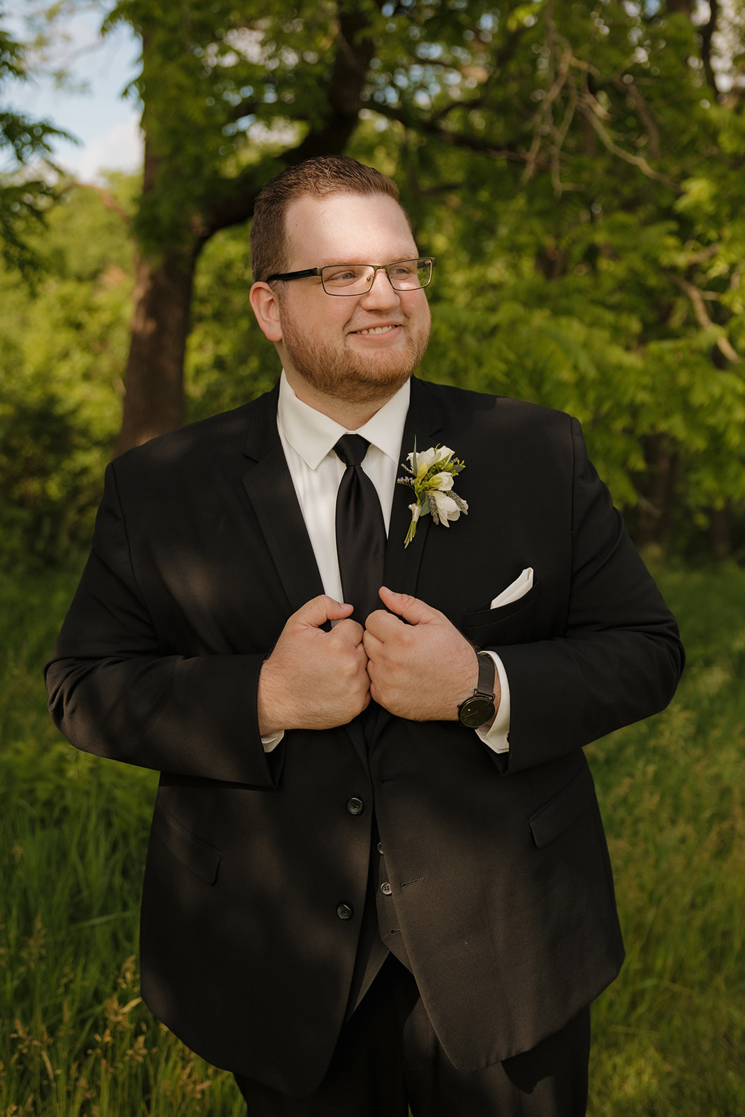 Groom adjusting black suit jacket during outdoor portrait session