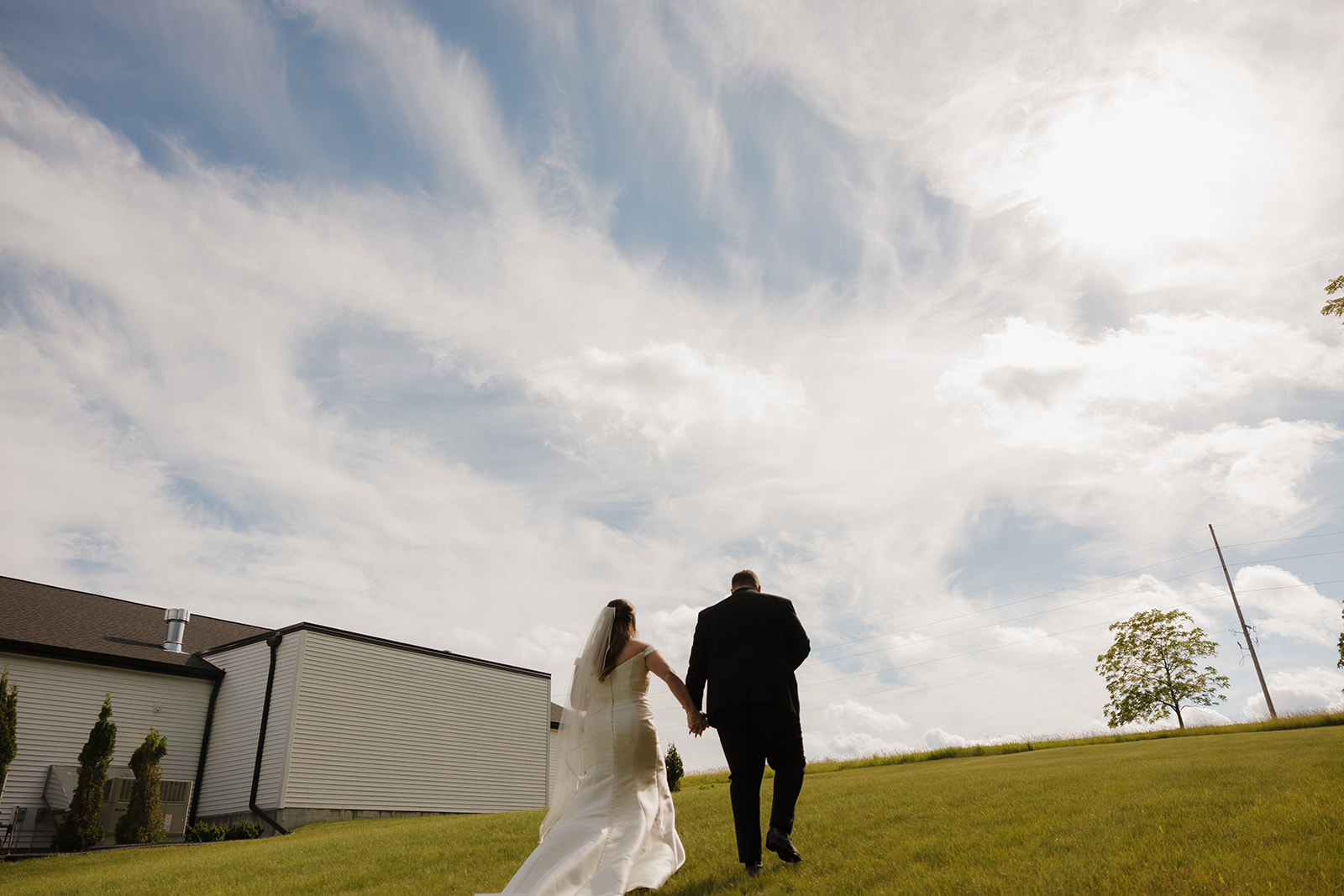 Bride and groom walking up grassy hill outside Wisconsin wedding venue