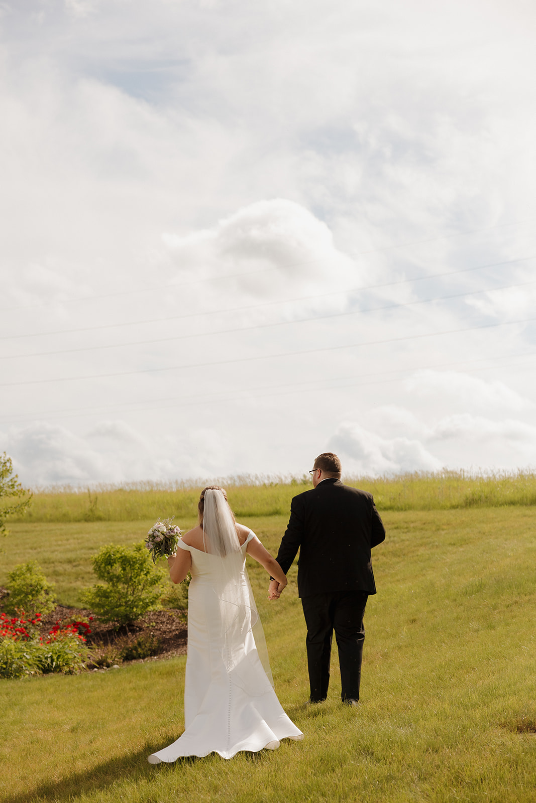 Bride and groom walking hand in hand across rolling hills at a Wisconsin wedding venue