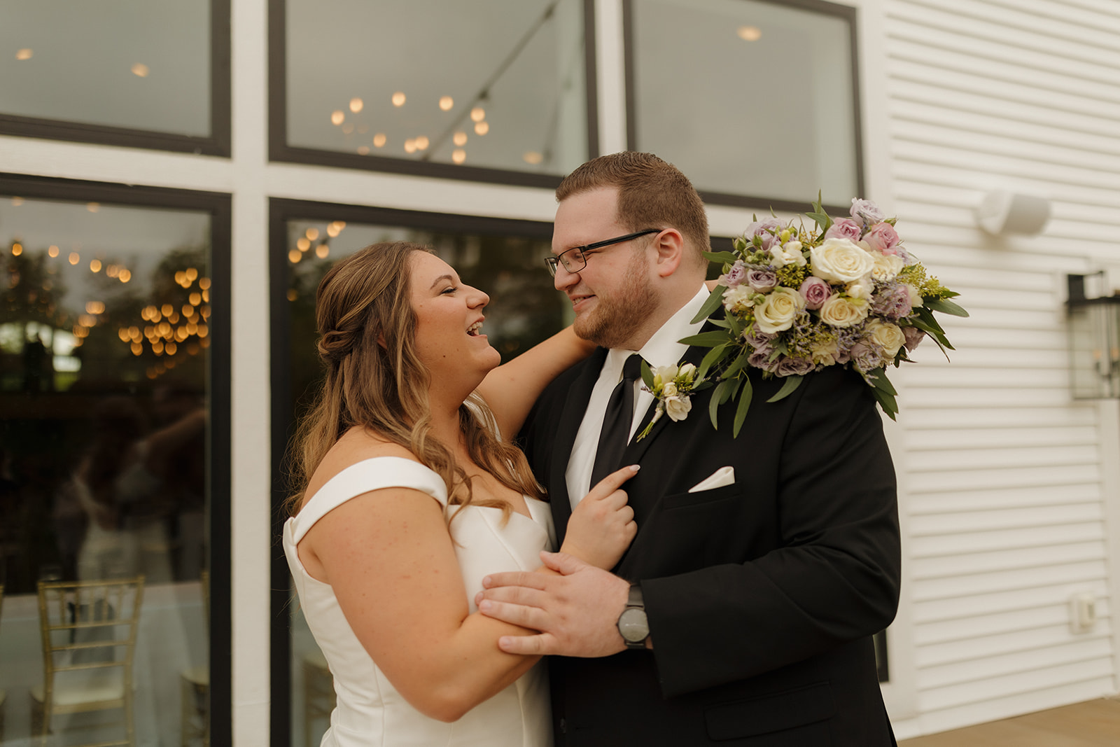 Bride and groom standing outside modern wedding venues in Wisconsin with large black-framed windows