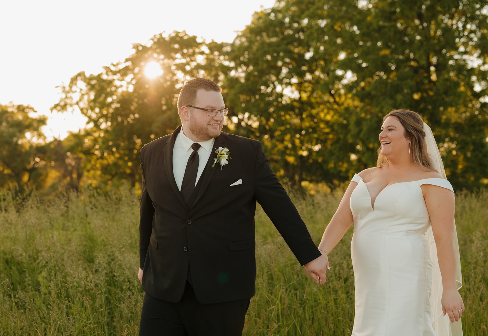 Bride and groom holding hands in golden field at sunset