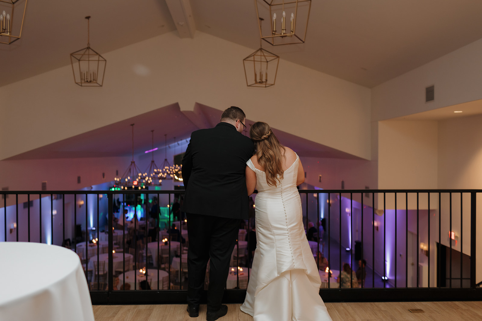 Couple overlooking reception space from balcony inside wedding venues in Wisconsin