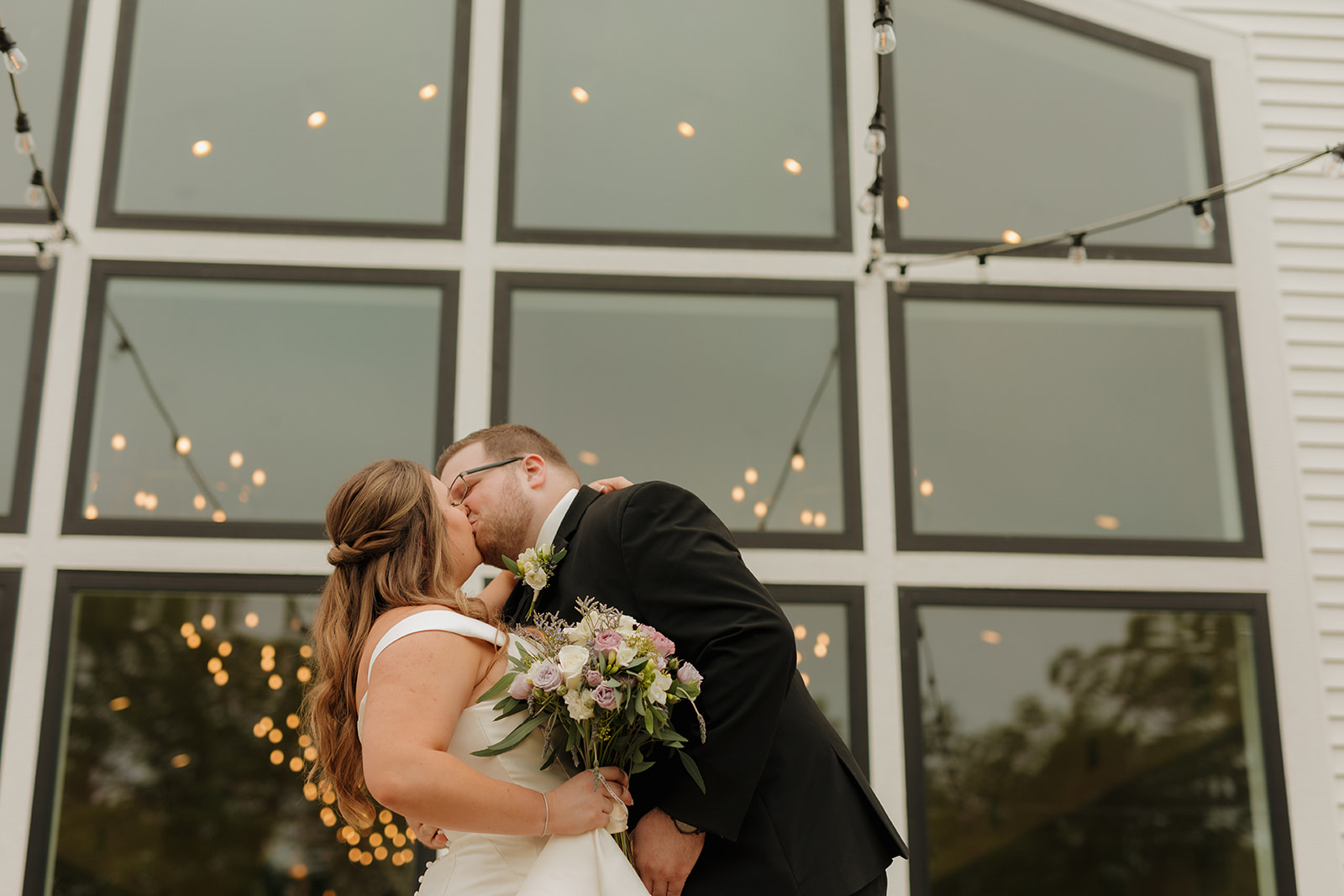 Bride and groom kissing beneath string lights at wedding venues in Wisconsin