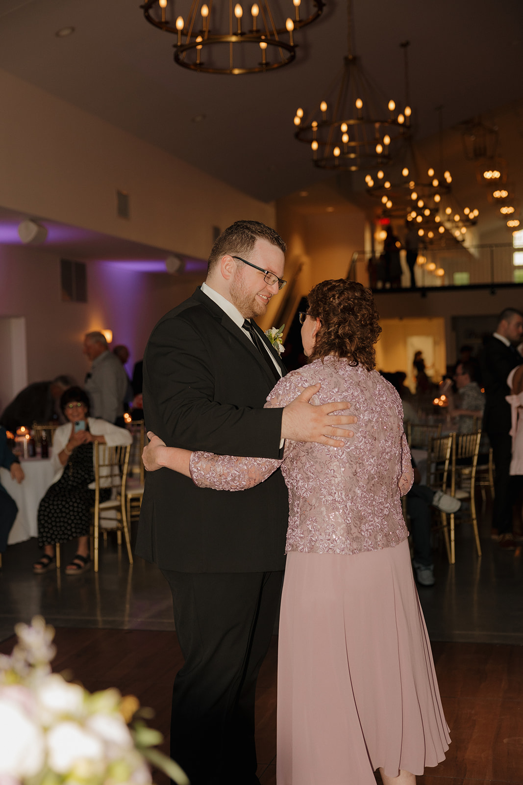 Groom dancing with family member under warm reception lighting