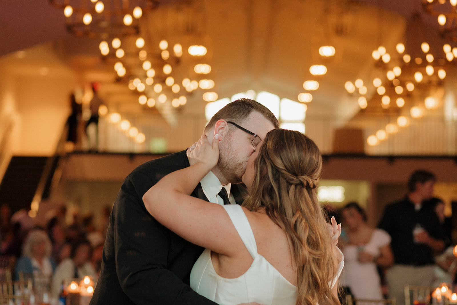 Bride and groom kissing on dance floor beneath chandelier lighting