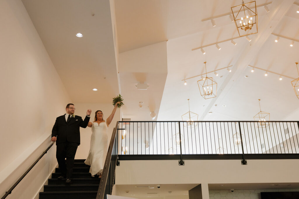 Bride and groom celebrating at top of staircase inside modern wedding venues in Wisconsin