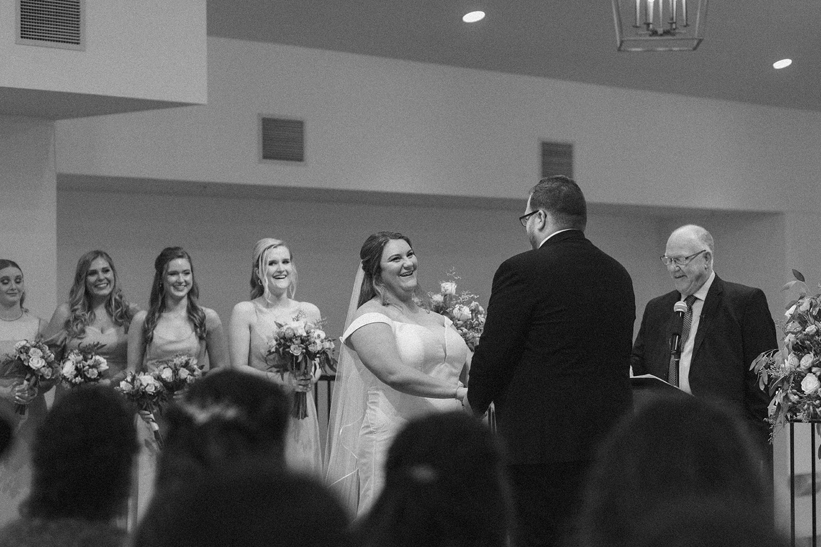 Black and white ceremony moment as couple holds hands at the altar