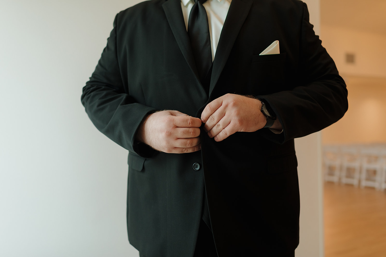 Groom buttoning black suit jacket in soft natural window light