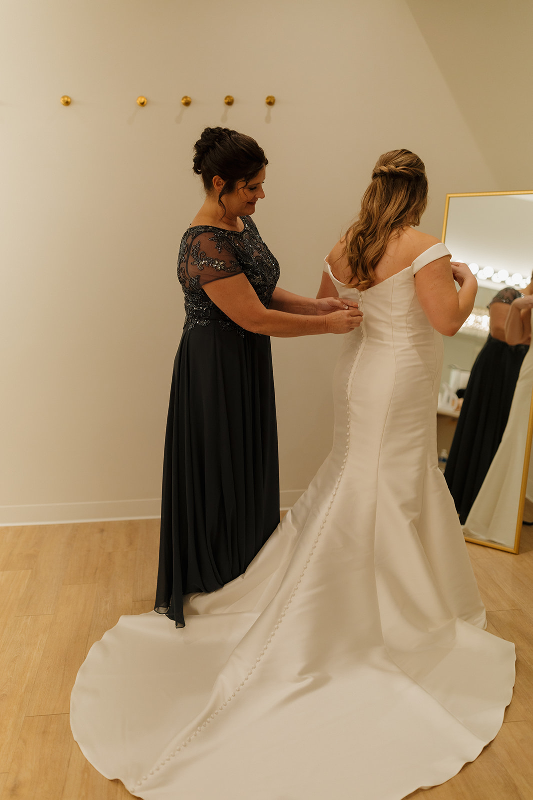 Mother helping bride button wedding dress in natural light bridal suite