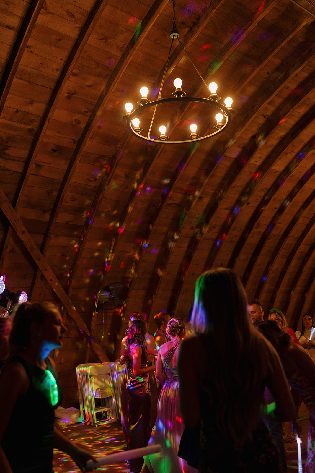 Dance floor filled with guests under disco lights and wooden rafters.