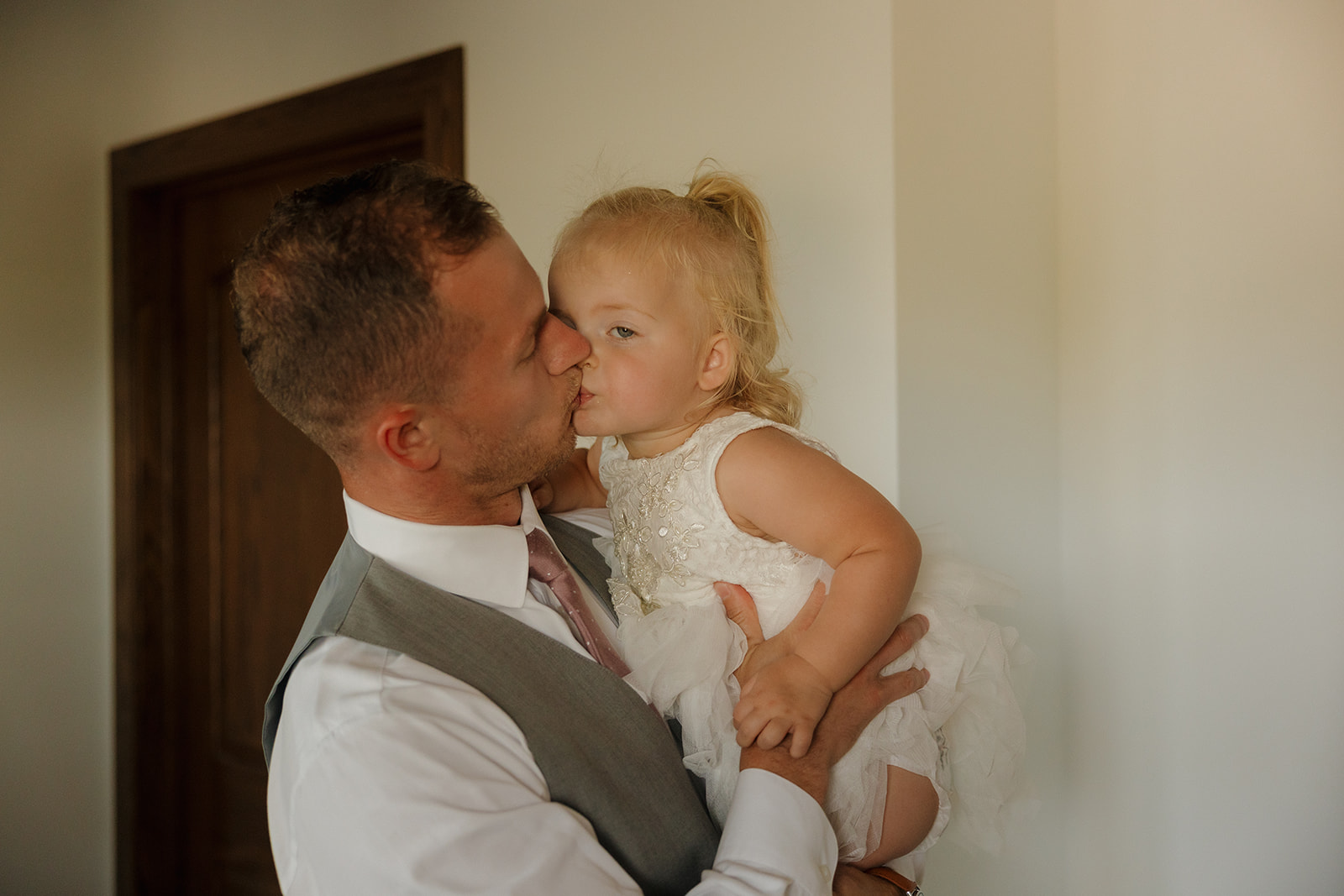 Groom kissing his young daughter on the cheek during a quiet pre-ceremony moment.