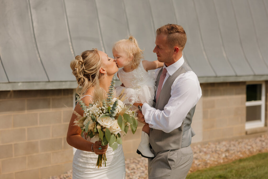 Bride kissing her daughter on the nose while groom holds her—heart-melting and checklist-worthy.