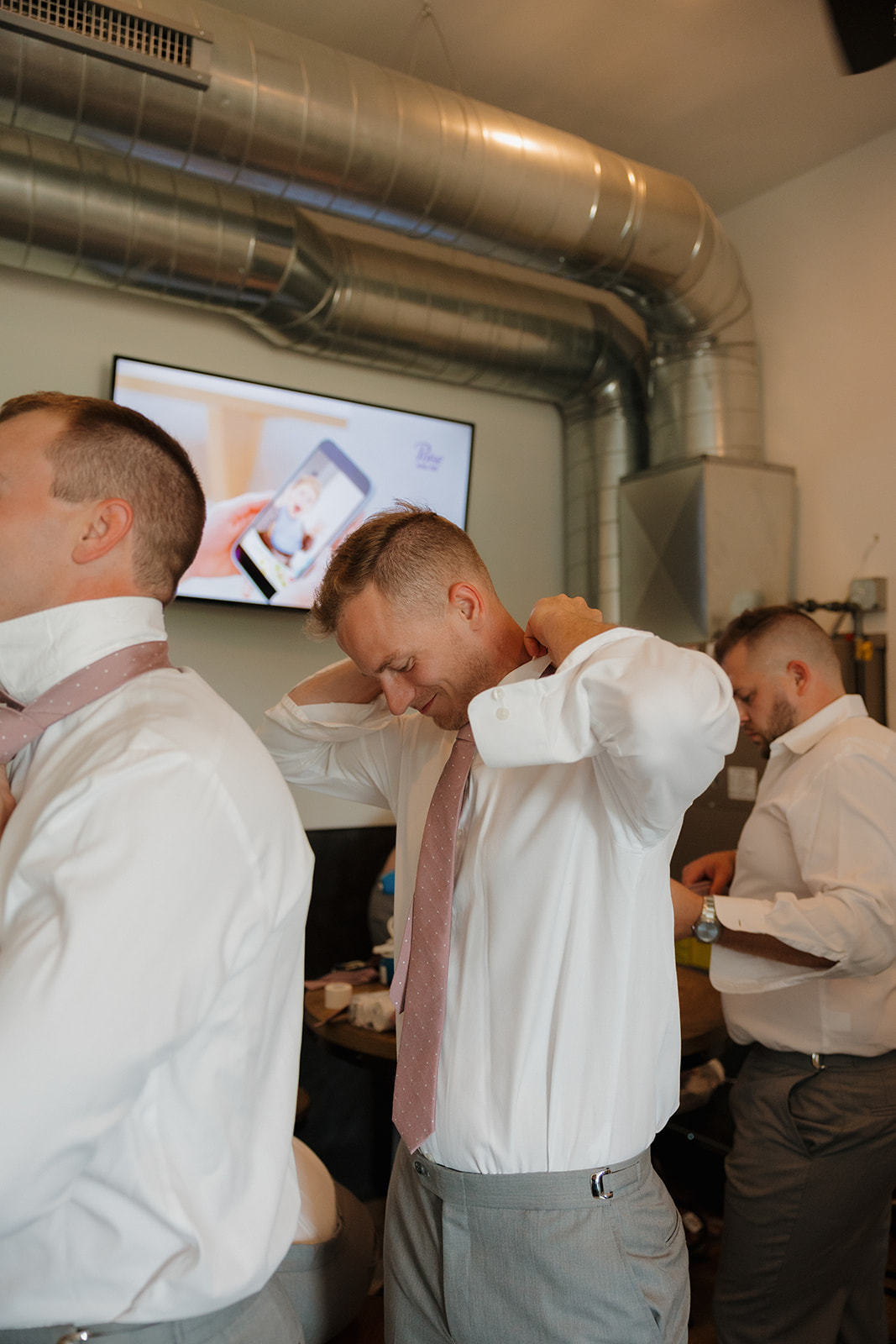 Groom adjusting his collar with groomsmen behind him as they prep for the day.
