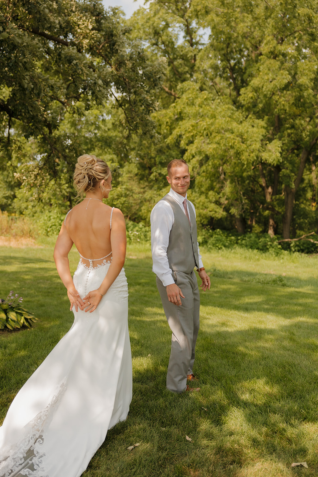 Bride approaching groom during their first look, with trees surrounding them in golden summer light.