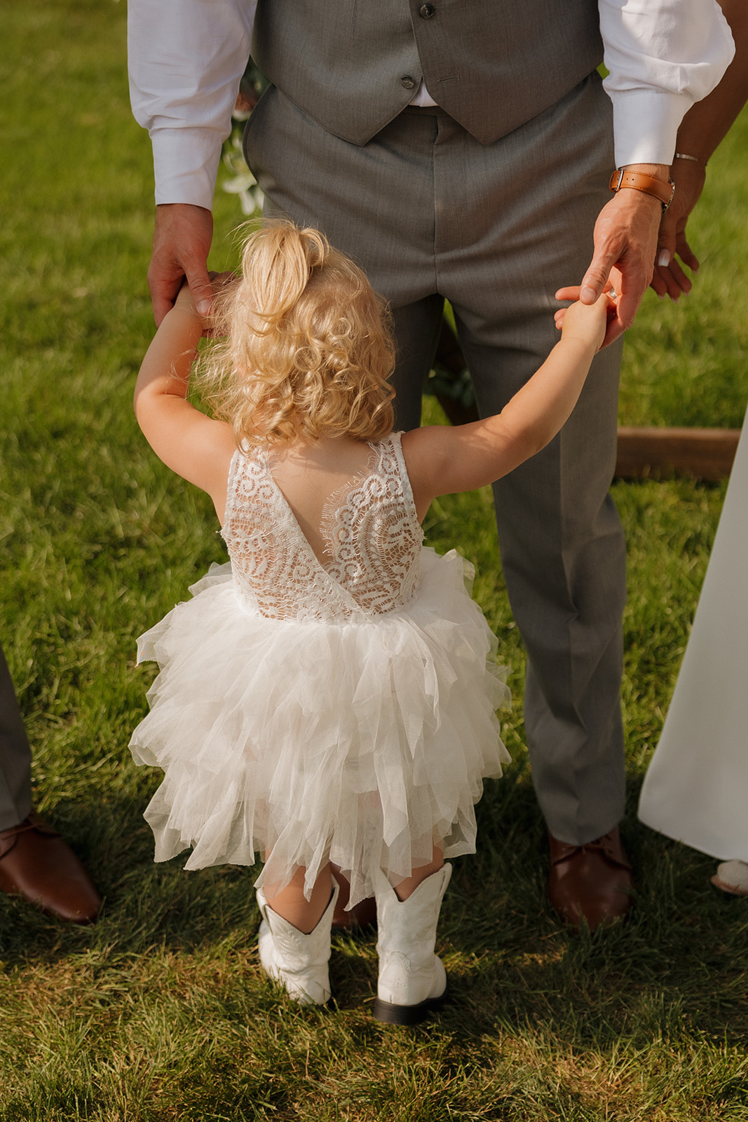 Close-up of the groom holding hands with his daughter in her white dress and cowboy boots.