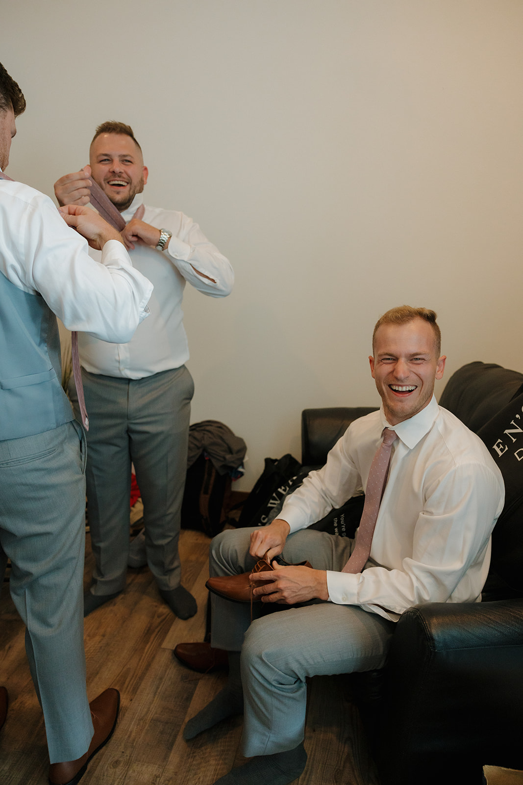 Groomsmen sharing laughs while getting dressed before the wedding ceremony.