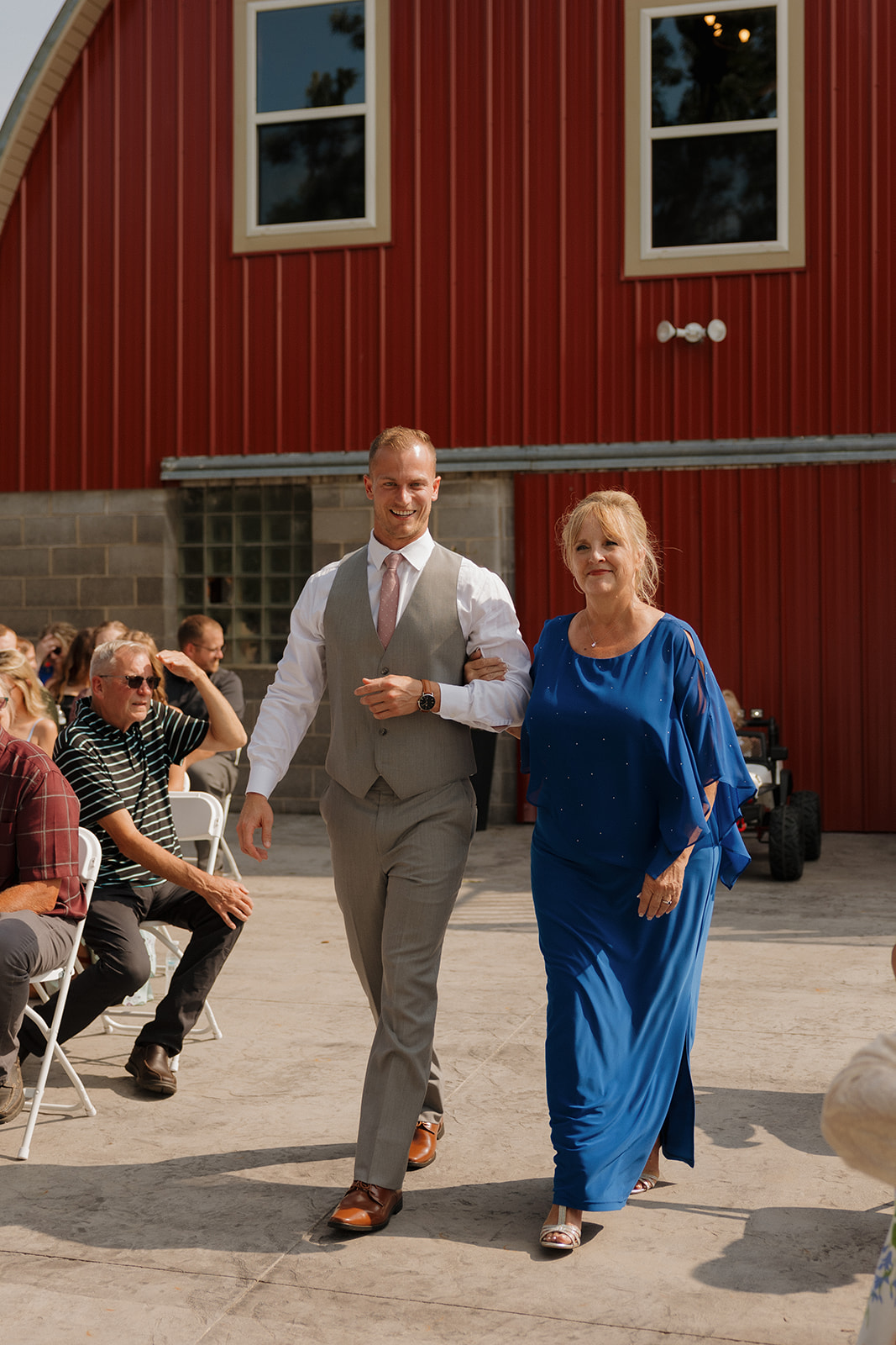 Groom walking his mother down the aisle outside the red barn at Prairie Creek Farm.
