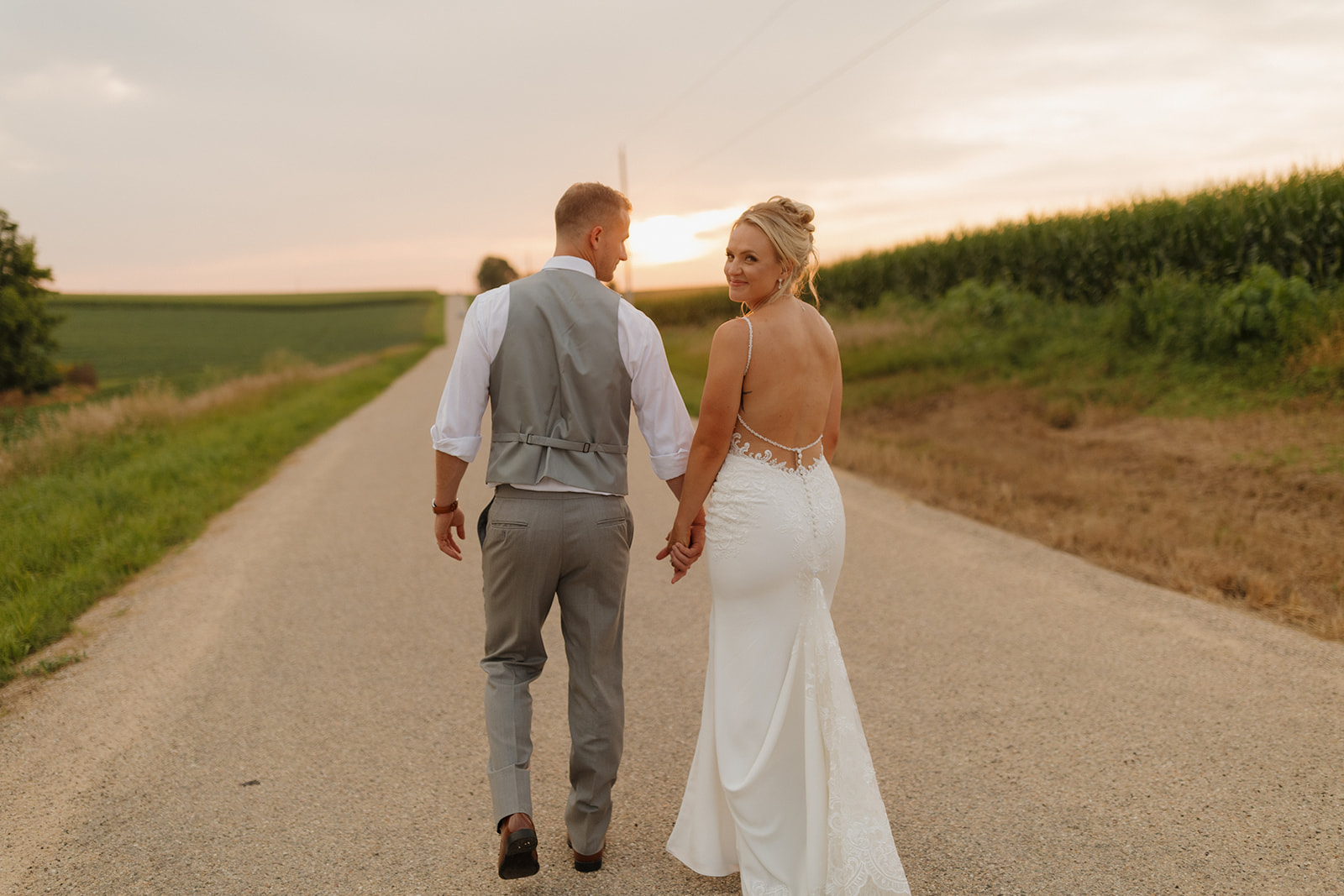Newlyweds walk hand in hand down a country road as golden hour fades behind them.